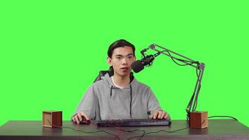 Young streamer broadcasting gameplay while he is sitting at workstation playing online action games with people. Young video blogger gaming live for stream at pc with microphone.