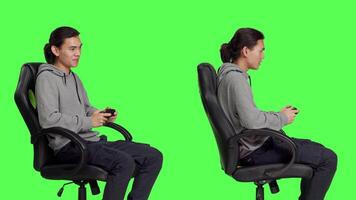 Young man playing videogames against greenscreen backdrop, sitting on chair and using controller on online gaming competition. Joyful relaxed guy having fun with rpg gameplay. video