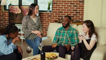 Asian woman telling entertaining story to friends at apartment party during weekend gathering. BIPOC group of people listening to interesting tale from host in living room video