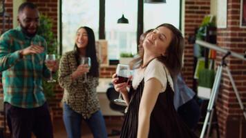 bipoc invitados bailando y hilado alrededor casa durante entretenido Departamento fiesta, contento amigos disfrutando optimista música, haciendo danza se mueve y Bebiendo vino a social reunión video