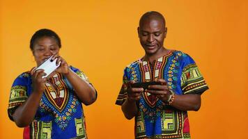 African american people playing videogames on mobile device, having fun with online gaming contest in studio. Married man and woman enjoying game tournament on smartphone app. video