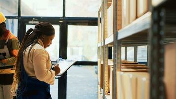 African american woman checking products on racks and shelves, using list on clipboard to do inventory in storage room. Female worker working with merchandise in warehouse space. photo