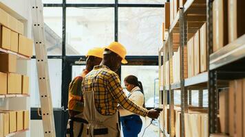 African american men working on supplies logistics with scanner and digital tablet, scanning merchandise with barcodes on racks. People doing stock inventory with storage room packs. photo