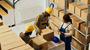 African american employees working on inventory and logistics, looking at stock list on clipboard to prepare merchandise for shipment. Storage room workers checking products in boxes. photo