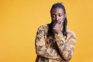 Confused person brainstorming business ideas, thinking at solution to solve difficult problem. Thoughtful african american man having unsure expression, standing in studio over yellow background photo