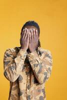 Male person doing three wise monkeys gesture on camera, covering eyes, mouth and ears as wisdom sayings. African american man advertising silence concept with hand in studio over background photo