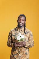 Smiling excited man holding white roses bouquet, presenting surprise for girlfriend at camera in studio over yellow background. African american boyfriend posing for valentine's day photo