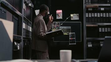 Police officer analyzing detective board with evidence, trying to solve crime or felony. Law agent doing detective work and catch suspect, using case files for investigation research. Handheld shot. photo