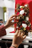Female worker arranging festive ornamental tree for festive decor all around retail store near racks, staff decorating place for christmas. African american woman putting decorations. Close up. photo