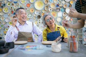 en el cerámica taller, un asiático retirado Pareja es comprometido en cerámica haciendo y arcilla pintura actividades. foto