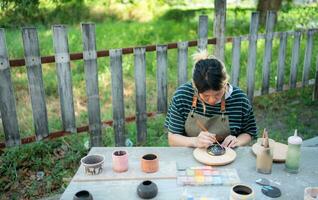 In the pottery workshop, Asian woman is engaged in pottery making and clay painting activities. photo