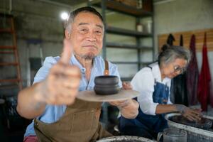 Portrait of senior craftsman working on pottery with thumb up photo