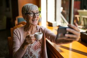 maduro mujer es sentado en café y relajante. ella es utilizando teléfono inteligente foto