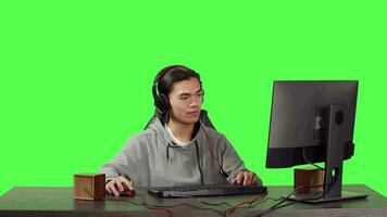 asiático jugador en computadora a ordenador personal, jugando web videojuegos con personas a través de el globo. joven persona teniendo divertido con juego de rol competencia, comunicado con amigos terminado pantalla verde. video