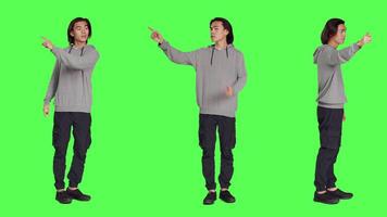 Model showing left or right directions in studio, pointing to both sides and indicating another path. Asian young adult advising someone to go that way, full body greenscreen backdrop. video