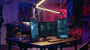 Panning shot of high tech computer system running malicious code in empty basement. PC monitors in empty neon lit criminal hideout used by hackers to commit illegal activities video