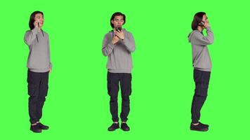 Modern guy talking on smartphone call over full body greenscreen, using telephone line to talk to his colleagues in studio. Young person answering call to have remote discussion. video