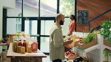 man välja eco Produkter till köpa, närmar sig handlare på Registrera till betala för väska av hemodlade producera. köpare håller på med matvaror handla på lokal- noll avfall eco affär. handhållen skott. video