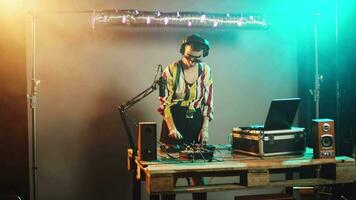 somnolent dj femme bâillement et en essayant à mélanger enregistrements à faire la fête, en buvant café à avoir certains énergie pour génial techno performance à boîte de nuit. artiste sentiment épuisé à stéréo platines. ordinateur de poche tir. video