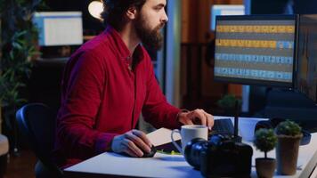 Photographer using software on computer to perform editing operations, enjoying cup of coffee while correcting images. Photo editor using PC to make adjustments to photographs in studio video