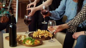 Close up shot of wine glasses being clinked at apartment party by BIPOC group of people celebrating their friendship together. Friends having reunion gathering, enjoying appetizers platter video