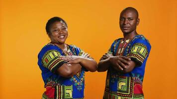 Confident ethnic couple posing in studio with colorful clothes, presenting traditional african american attire and being proud about their culture. Smiling husband and wife with arms crossed. video