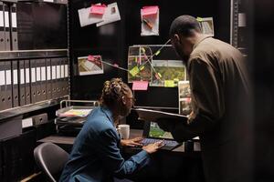 Detectives analyzing case file and searching information on laptop while working late in agency office. Investigators reading csi report and checking crime scene photos on computer screen