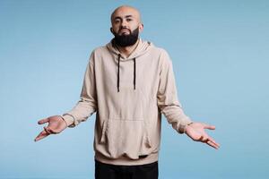 Arab man shrugging shoulders in doubt and confusion while looking a camera. Young person spreading arms in questioning gesture and making do not know signal studio portrait photo