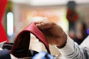 Employee arranging ties and accessories in box for store display, counting merchandise in clothing store. African american sales manager handling festive decorations, clothes inventory. Close up. photo