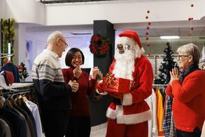 empleado anuncia rifa ganador nombres en ropa almacenar, preparando a dar gratis ropa como premio a persona. Papa Noel claus hombre extensión Navidad espíritu a centro comercial, impaciente clientes. foto