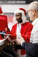 Worker presenting ties to senior man, recommending accessories for christmas eve festivity formal attire. Assistant dressed as santa claus talking to customer about fabric quality and outfits. photo