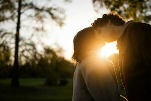Portrait of happy loving couple in park in sunset. Couple in silhouette kissing. photo