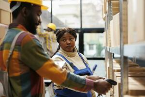 African american storehouse manager looking at worker scanning parcels. Man and woman warehouse employees checking packages barcodes, doing goods inventory in storage room photo