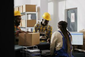 Postal service worker examining packed parcel before delivery at checkout. Warehouse handlers and operator managing package dispatching and checking client orders list on computer photo