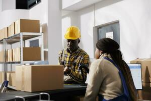 African american man and woman storehouse coworkers chatting at storage room counter desk. Postal service employees discussing parcel dispatching at post office reception table photo