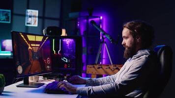 Portrait of smiling man in dark living room playing engaging video games on gaming PC at computer desk, chilling after work. Happy gamer contending against foes in online multiplayer shooter