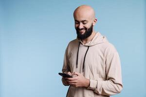 Smiling arab man typing message on smartphone, having fun online communication. Cheerful carefree person texting online while using social media application on mobile phone photo