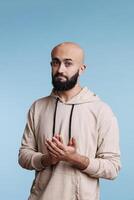 Arab man clapping hands and looking at camera with respect facial expression. Young person with proud emotions applauding and congratulating with success studio portrait on blue background photo