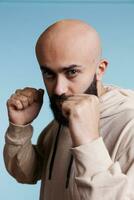 Arab man showing strength while standing with clenched fists in boxing position portrait. Young person making fighter gesture while looking at camera with aggressive facial expression photo