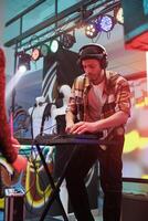 Performer playing techno music at discotheque in nightclub. Young man dj in headphones using digital controller for mixing sound on stage with spotlights at party in club photo