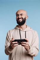 emocionado árabe hombre riendo mientras jugando en línea juego utilizando teléfono inteligente aplicación sonriente jugador disfrutando móvil videojuego en teléfono y mirando lejos con alegre contento facial expresión foto