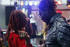 Young couple dancing together while partying and relaxing in nightclub. African american man and woman moving to music sound on dancefloor while attending social gathering in club photo