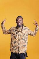 Grumpy young adult having nervous expression on face while standing in studio over yellow background. Upset disappointed african american man feeling angry and furious, having mental breakdown photo