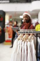 Selective focus of retail worker reviewing list of fashion items for stock inventory, working at mall during holiday season. African american employee managing logistics on tablet, xmas decor. photo