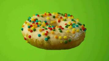 heerlijk zoet donut roterend Aan een bord. helder en kleurrijk besprenkeld donut Aan een groen achtergrond. detailopname. 4k video