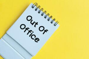 Out of office text on notepad with yellow background. Out of office concept photo