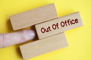 Finger pushing out wooden block with out of office text on yellow cover background photo