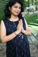 A pregnant Indian lady poses for outdoor pregnancy shoot and hands on belly, Indian pregnant woman puts her hand on her stomach with a maternity dress at society park, Pregnant outside maternity shoot photo