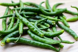 Fresh Green chili pepper on plain wooden table, green essential vegetables for all essential foods, view of unpeeled vegetables with plain background photo