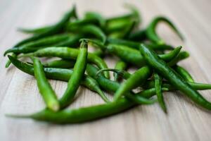 Fresh Green chili pepper on plain wooden table, green essential vegetables for all essential foods, view of unpeeled vegetables with plain background photo